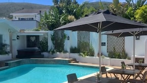 Una piscina con solárium alicatado, mobiliario exterior y una zona cubierta con sombrilla.