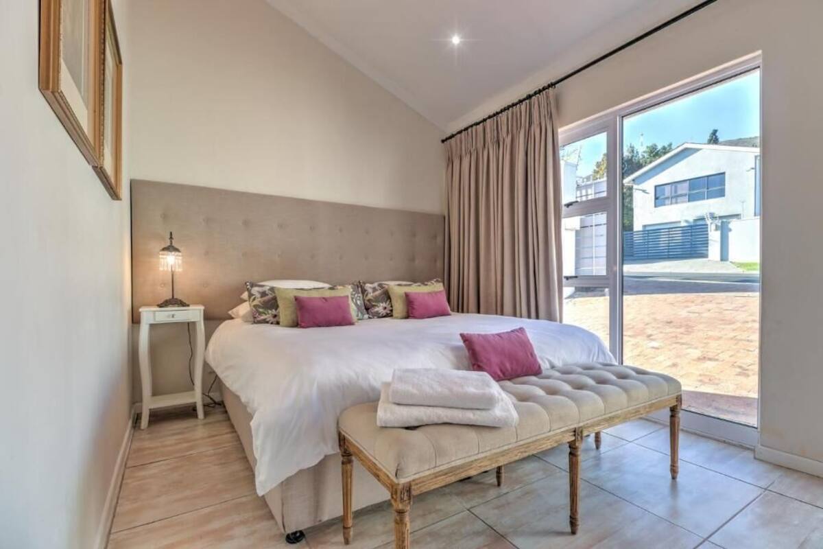 Un dormitorio con una cama grande, una mesita de noche, un banco y vistas al exterior.