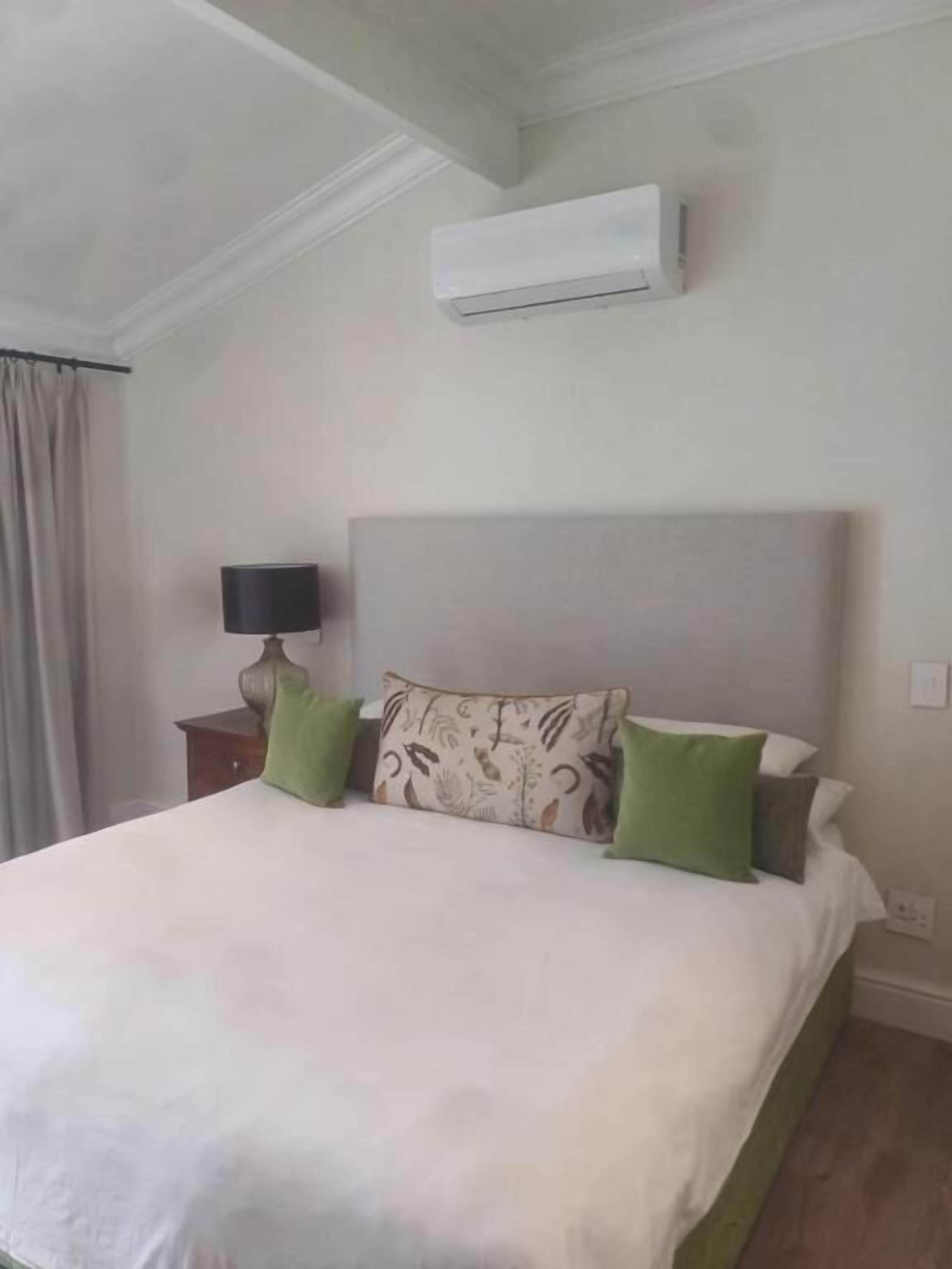 A neatly made bed with a patterned pillow, a bedside lamp, and an air conditioning unit on the wall.