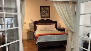A bedroom with a wooden bed, a nightstand, a lamp, and a window with curtains. - Historic Cigar Barons Mansion (Key West)