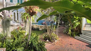 A garden pathway with a bird, lush greenery, and a building with white walls and green shutters. - Historic Cigar Barons Mansion (Key West)
