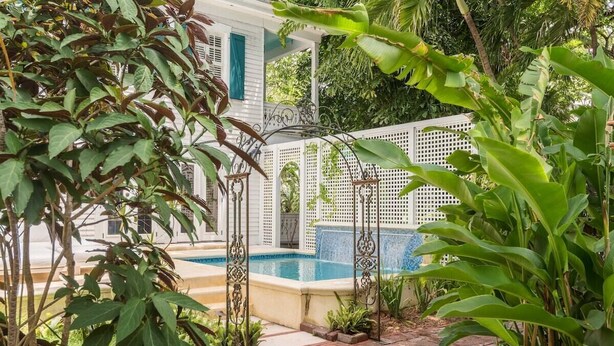A pool area with a white fence, a small waterfall feature, and lush greenery. - Historic Cigar Barons Mansion (Key West)