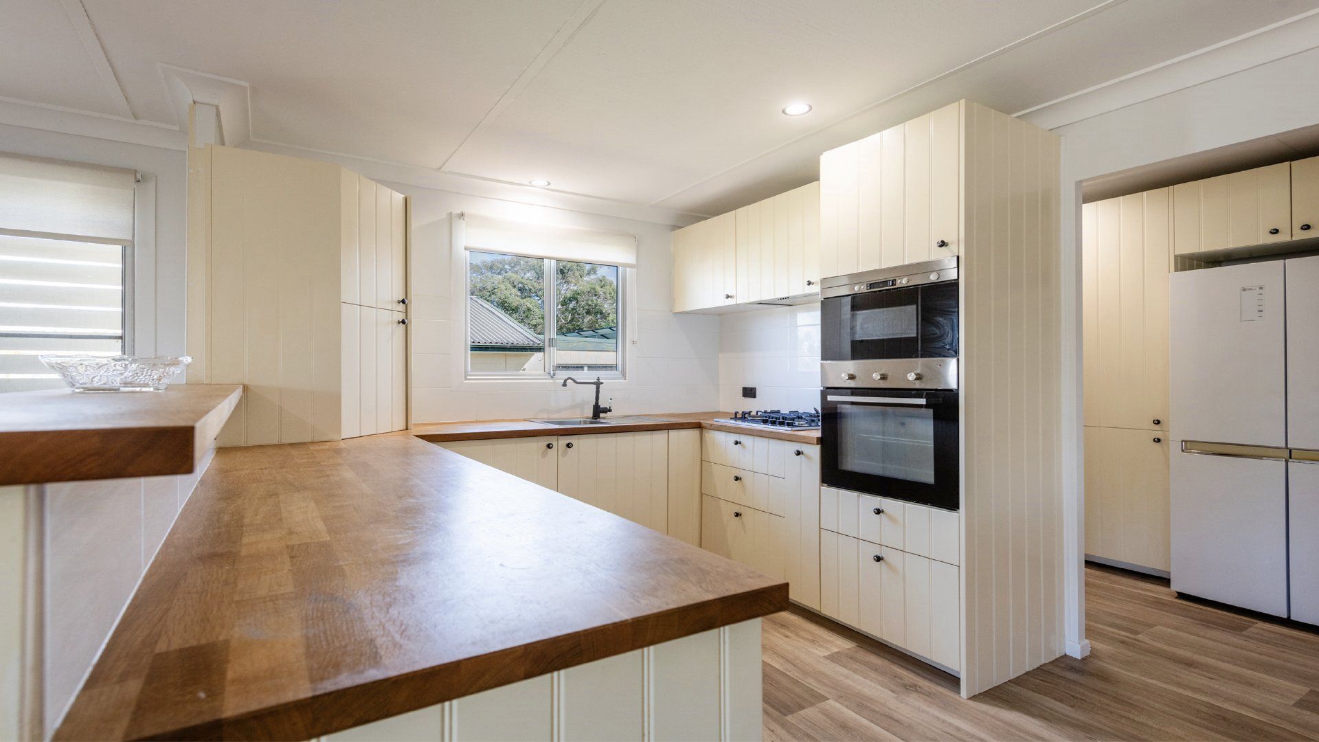 Una cocina moderna con armarios blancos, encimera de madera, horno empotrado y una ventana que deja entrar luz natural.