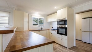 A modern kitchen with white cabinetry, a wooden countertop, a built-in oven, and a window providing natural light.