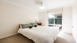 A bedroom with a bed, a nightstand, a lamp, and a sliding glass door leading to an outdoor area. - Cookies Hideway - Coastal holiday vibes. (WOOLI)
