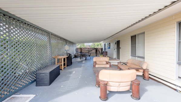A covered outdoor patio with a seating area, a table, and a grill.