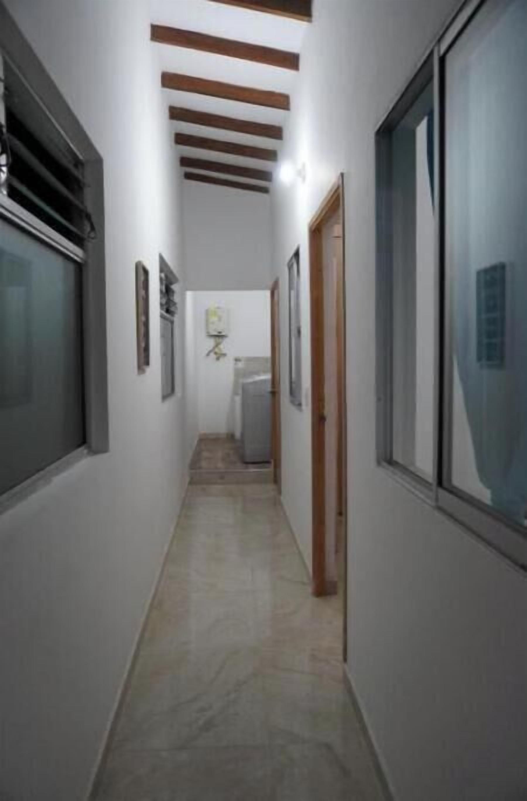 A narrow hallway with a tiled floor, wooden beams on the ceiling, and a door on the right.