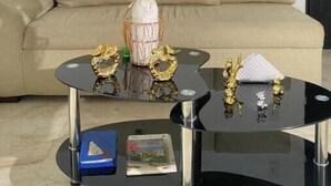 Ein Wohnzimmer mit einem beigefarbenen Sofa, einem Glastisch mit Dekoration und einem an der Wand hängenden Kunstwerk.