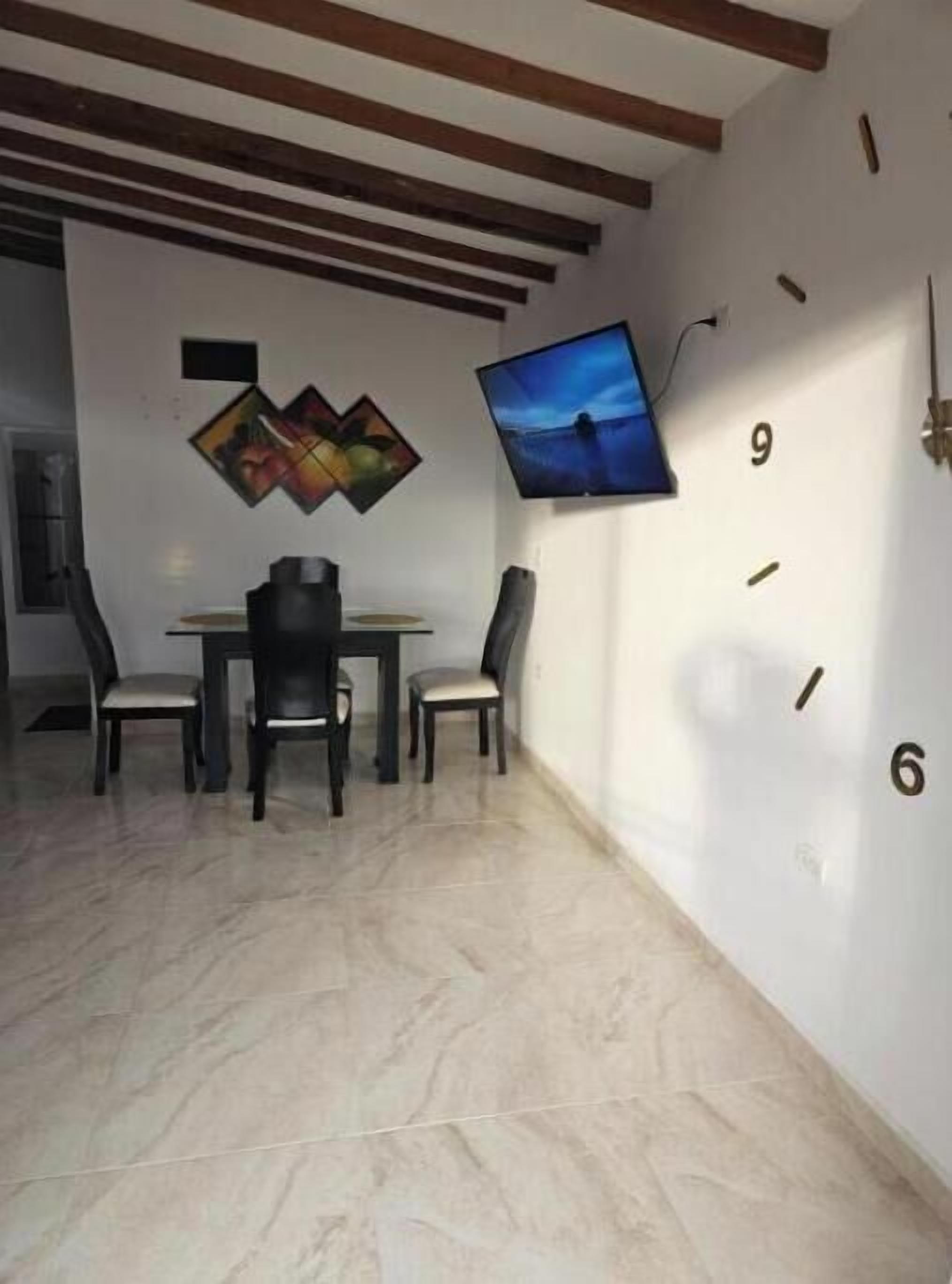 A dining area with a table and chairs, a wall-mounted TV, and a clock.