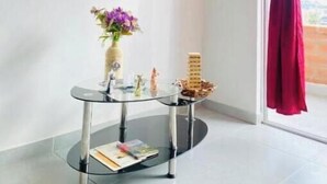 Ein modernes Zimmer mit einem Wand-Fernseher, einem Glastisch mit Blumenvase und einem Fenster mit roten Vorhängen.