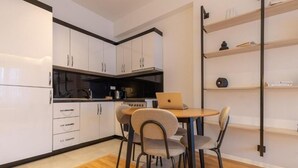 A modern kitchen with white cabinets, a wooden dining table, and chairs. - Prishtina City Apartments 2 (Pristina)