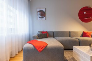 A modern living room with a grey sofa, red cushions, and a framed abstract artwork on the wall. - Prishtina City Apartments 2 (Pristina)