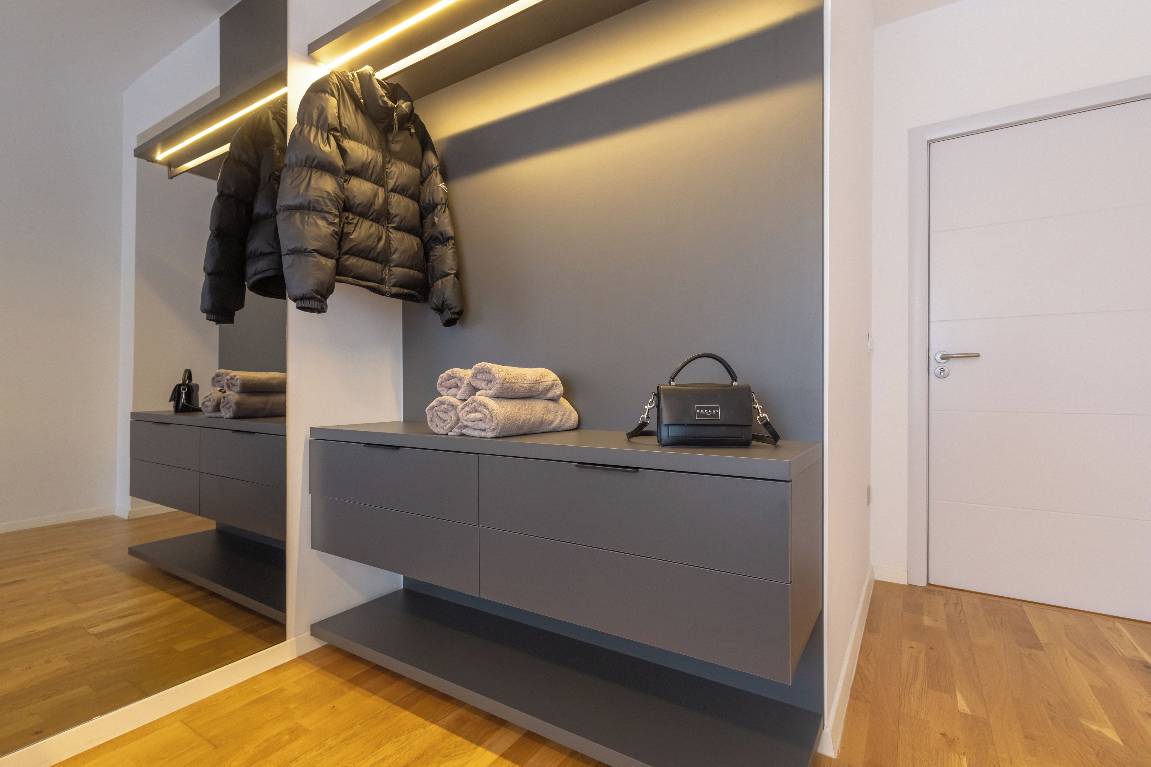 A modern bathroom with a grey vanity, a towel rack, a puffer jacket, and a handbag.
