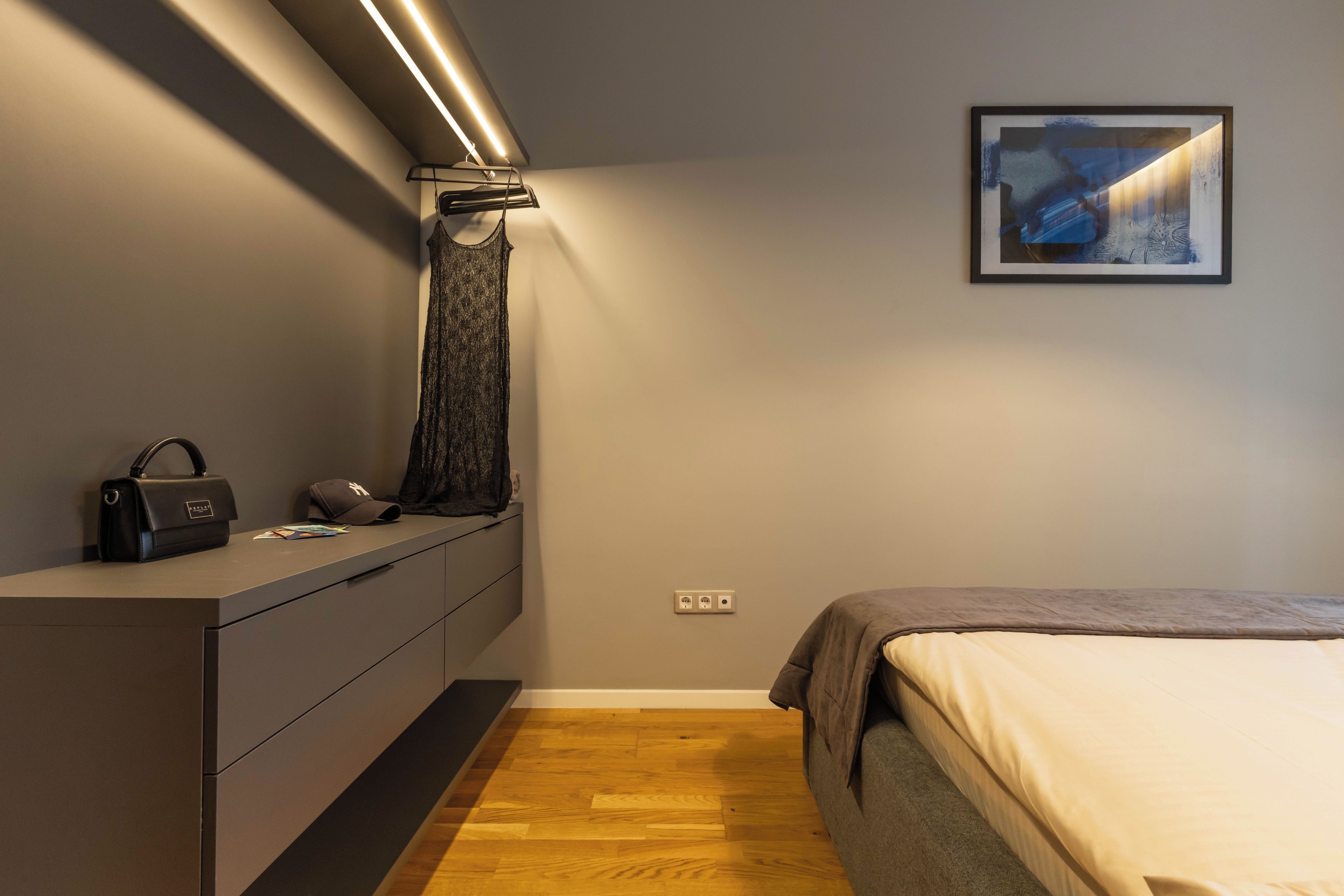 Una camera da letto con un letto, una cassettiera, un appendiabiti, un quadro incorniciato a parete e una lampada.