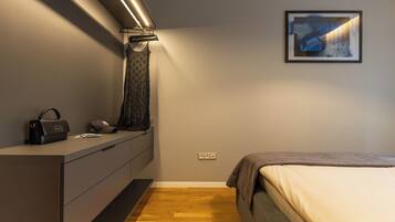 Una camera da letto con un letto, una cassettiera, un appendiabiti, un quadro incorniciato a parete e una lampada.