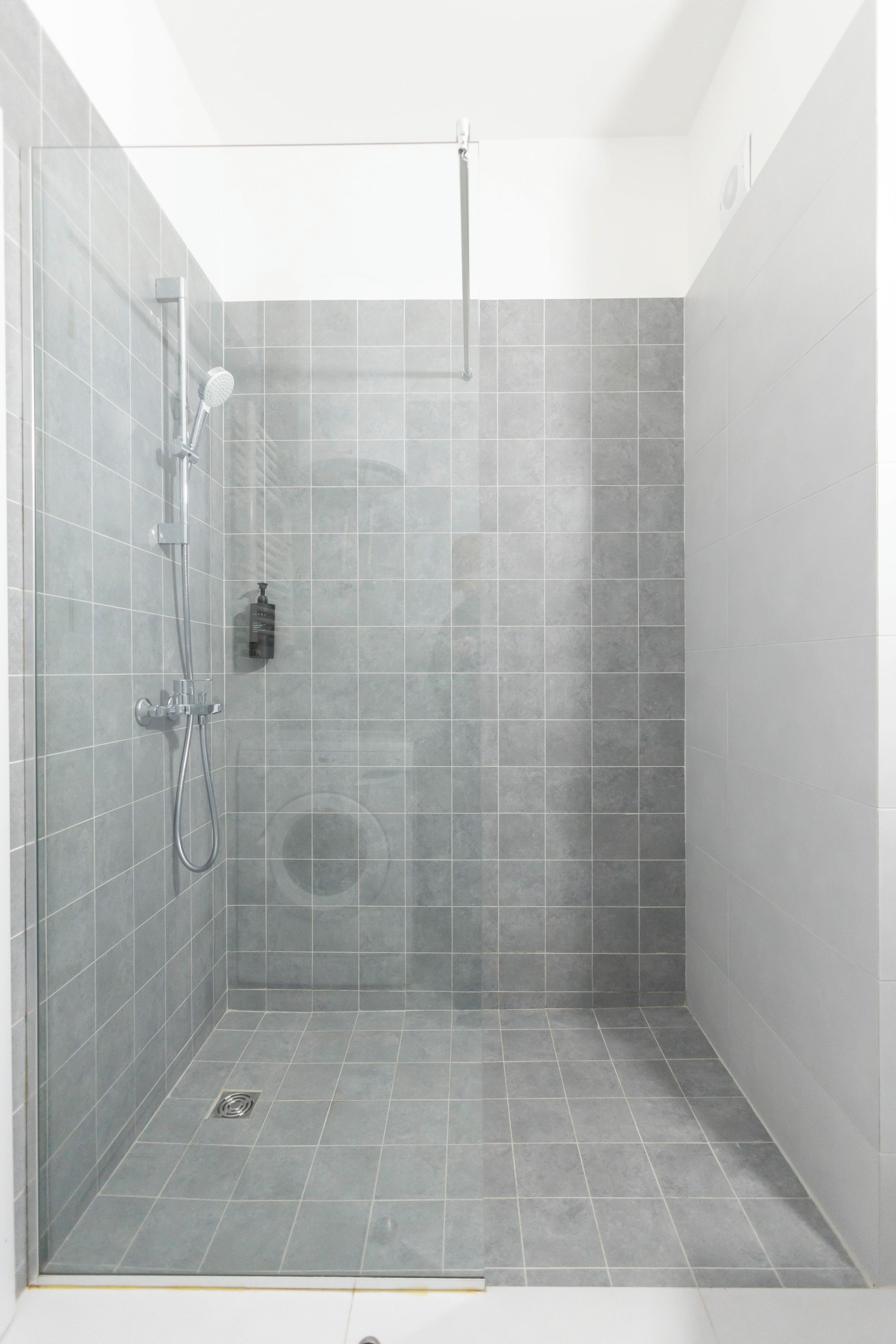 A shower with a handheld showerhead and a wall-mounted faucet.