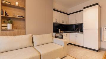 A modern living room with a beige sofa, a coffee table, and a kitchen area with white cabinets and a black countertop.