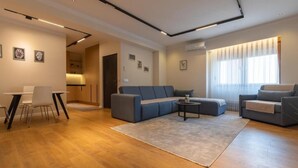 A modern living room with a sofa, a dining table with chairs, a coffee table, and a large window with curtains. - Prishtina City Apartments 2 (Pristina)