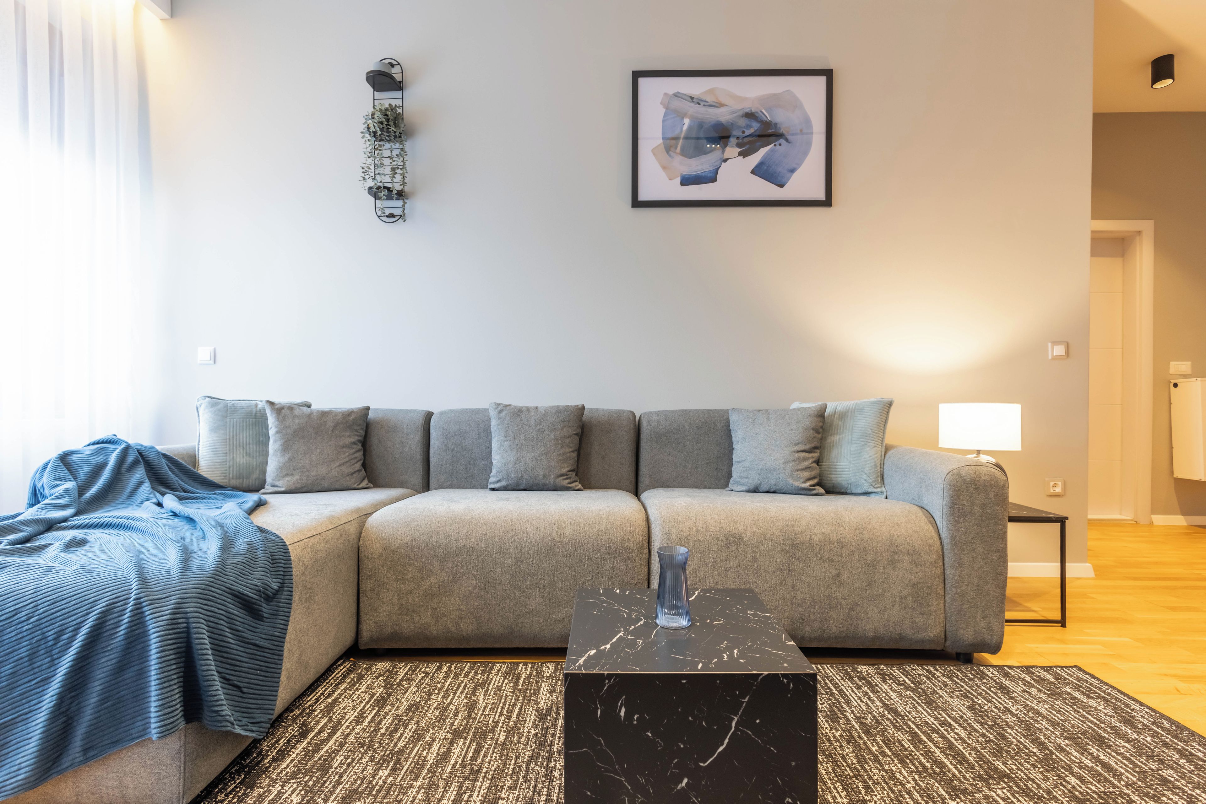 A modern living room with a grey sofa, a black marble coffee table, and a patterned rug.