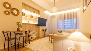 A modern living room with a sofa, a TV mounted on the wall, a dining table with chairs, and a small side table. - Prishtina City Apartments 2 (Pristina)