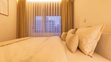 Habitación de hotel con una cama grande, cortinas color beige y vista a edificios por la ventana.