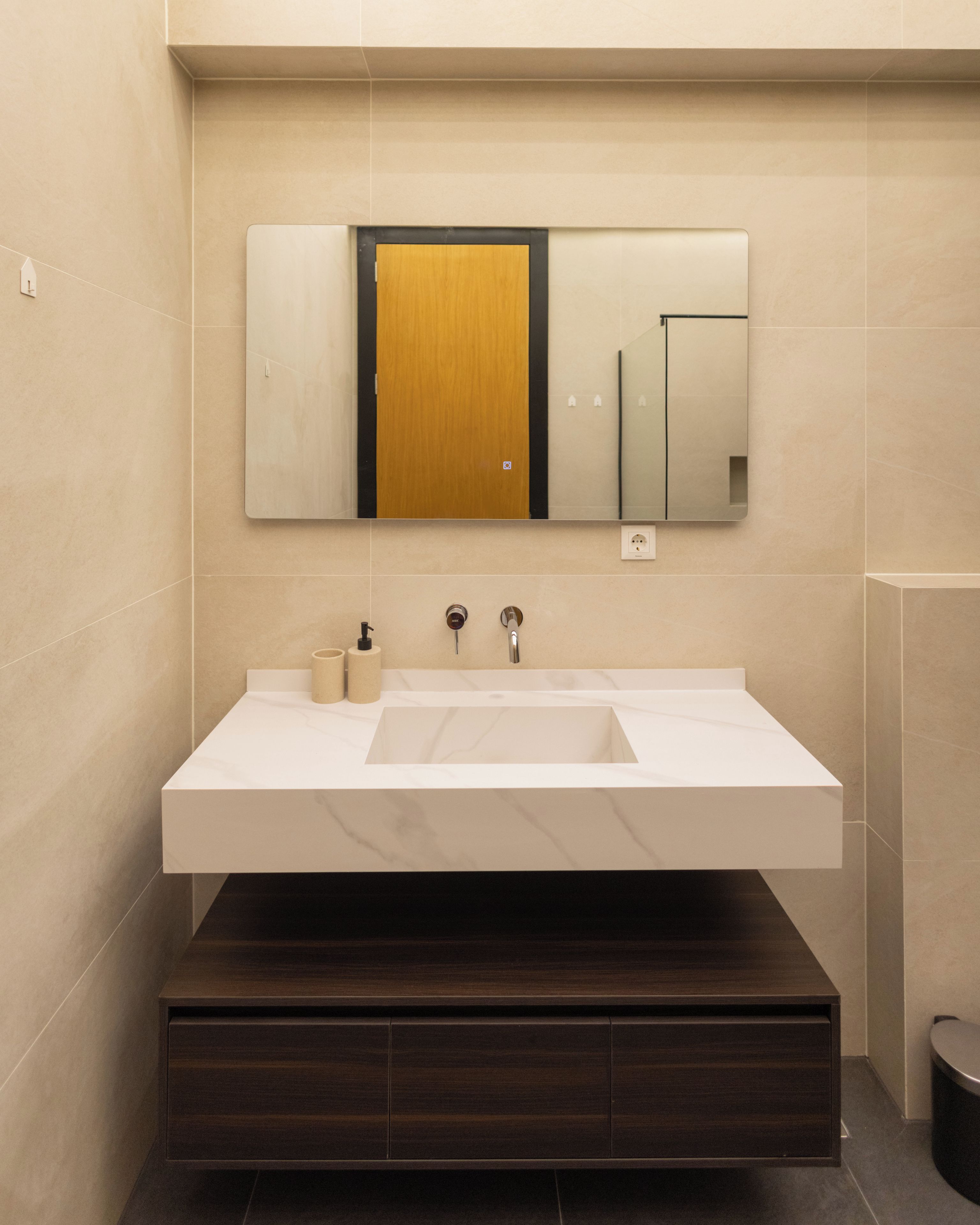Un baño moderno con un lavamanos blanco grande, una puerta de madera y un espejo encima.
