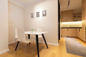 A modern dining area with a white table and chairs, a small plant on the table, and a kitchen area with cabinets and a countertop. - Prishtina City Apartments 2 (Pristina)