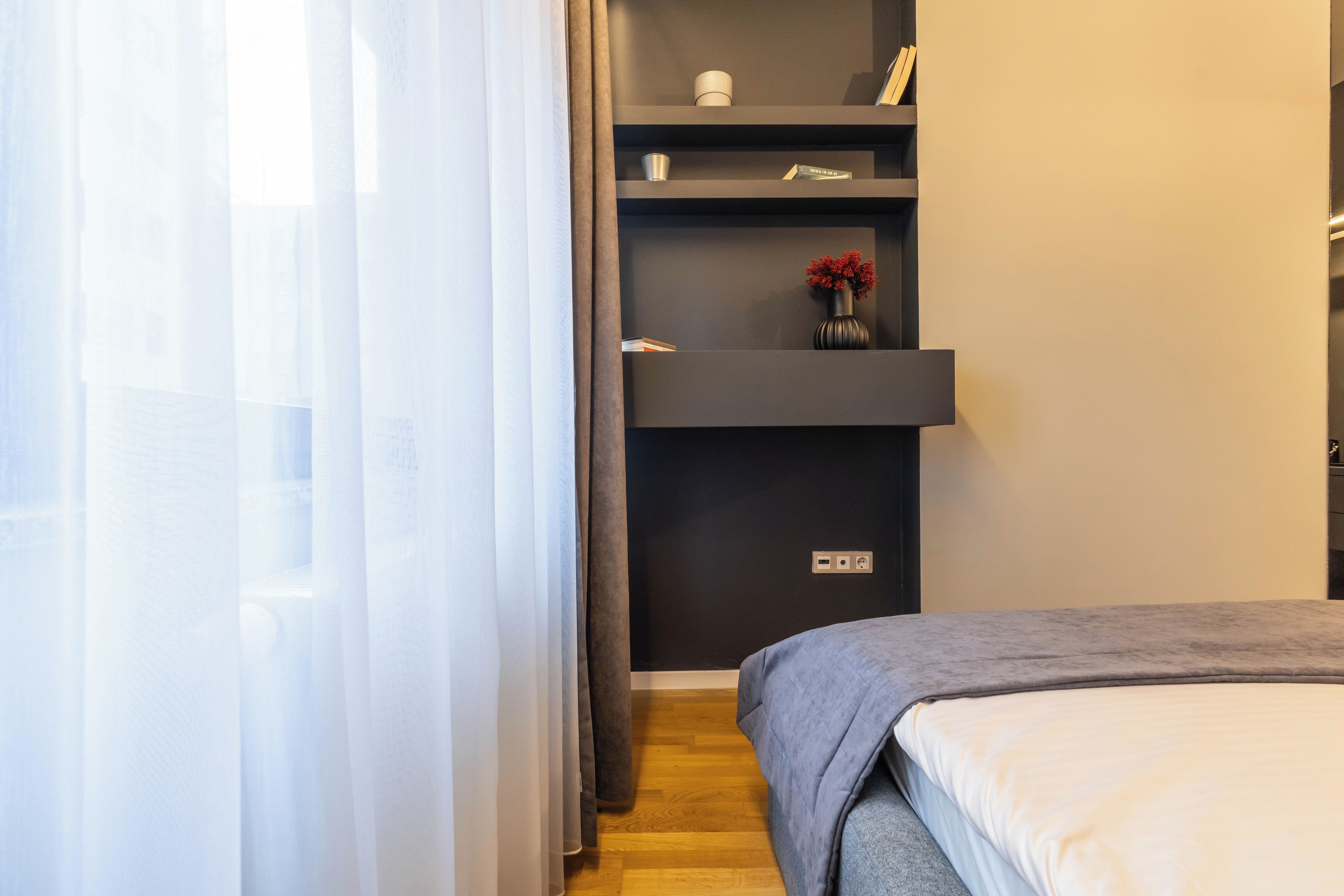 Une chambre avec un lit, une étagère avec des livres et un vase, et une prise électrique sur le mur.