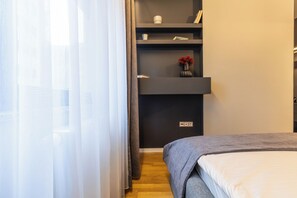 Une chambre avec un lit, une étagère avec des livres et un vase, et une prise électrique sur le mur.