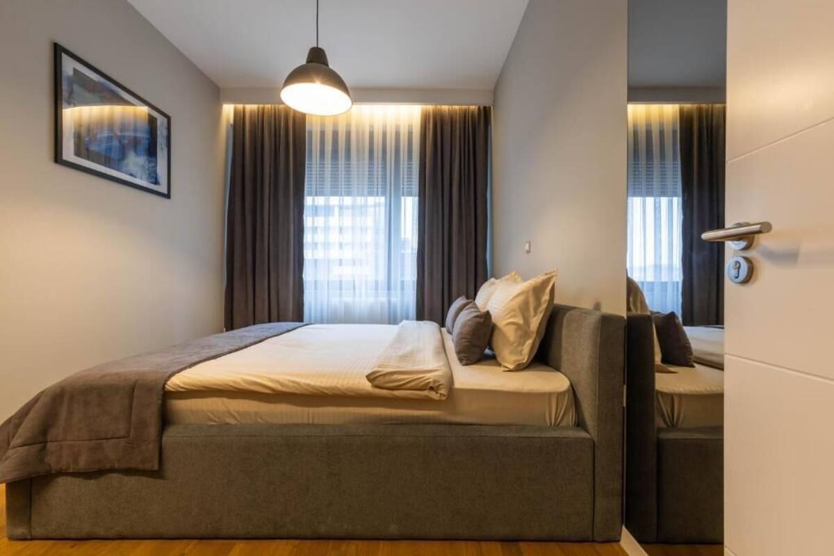 Moderni hotellihuone, jossa on suuri sänky, yöpöytä, riippuvalaisin ja ikkuna, jossa on verhot.