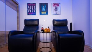 A room with two black leather chairs, a small round table with bottles and snacks, and three posters on the wall. - Prishtina City Apartments 2 (Pristina)