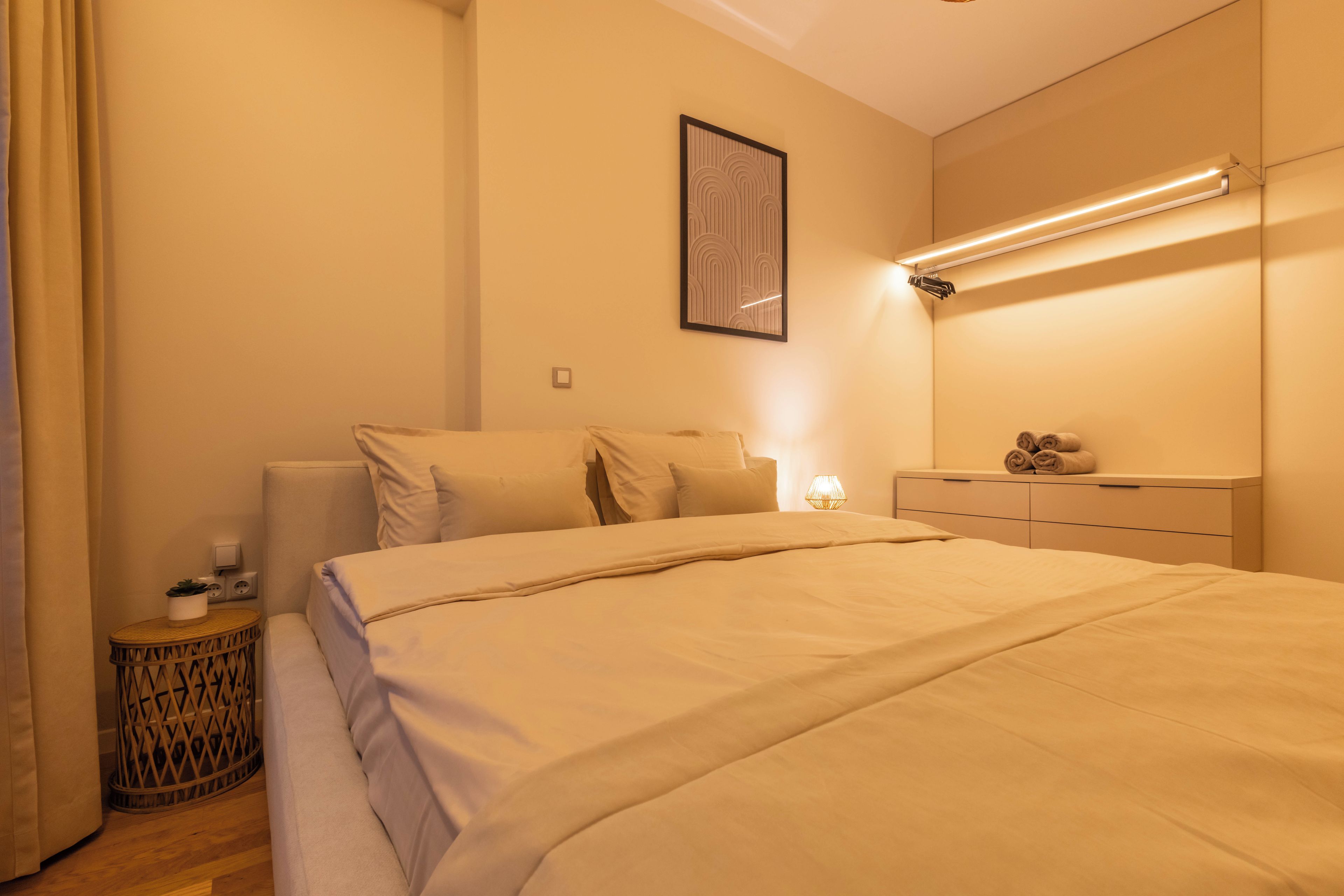 Un dormitorio con cama, mesitas de noche, una lámpara de pared y un cuadro enmarcado.