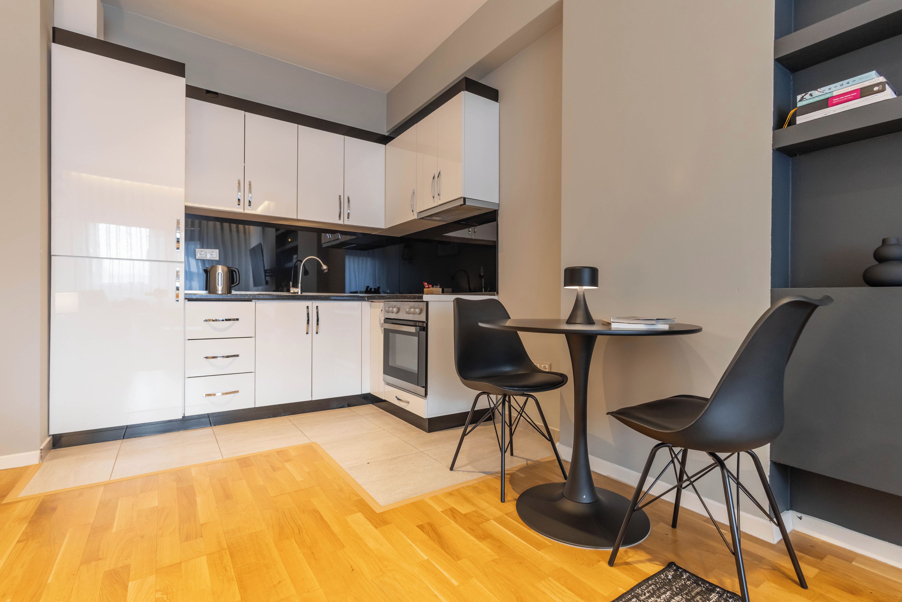 A modern kitchen with white cabinets, a built-in oven, and a dining area with two black chairs and a table.