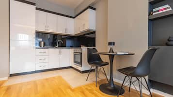 A modern kitchen with white cabinets, a built-in oven, and a dining area with two black chairs and a table.
