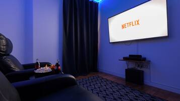 Een moderne woonkamer met een grote flatscreen televisie aan de muur, een leren bank, een bijzettafeltje met lekkernijen en een kamerbreed tapijt.