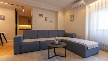 Una sala de estar moderna con un sofá seccional, una mesita redonda y una zona de cocina al fondo.