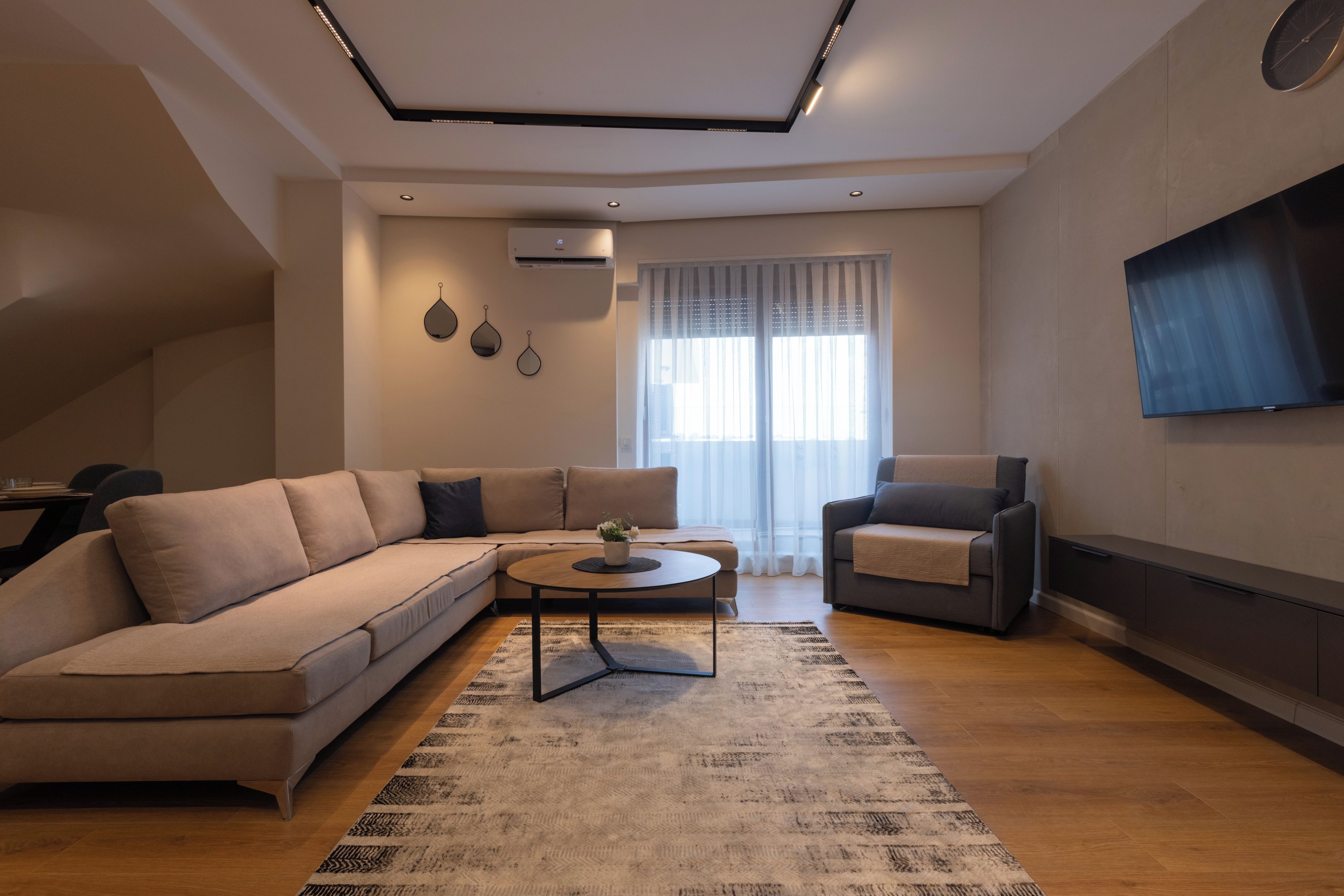 Una sala moderna con un sofá seccional, una mesa de centro y un televisor montado en la pared.