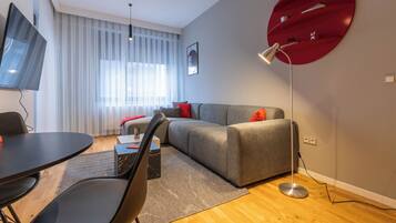 Een moderne woonkamer met een grijze bank, een ronde rode bijzettafel, een zwarte eettafel en een vloerlamp.