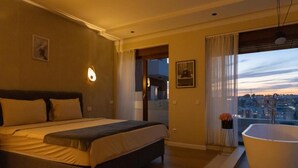 A bedroom with a bed, a bathtub, a city view, and a door leading to a balcony. - Prishtina City Apartments 2 (Pristina)