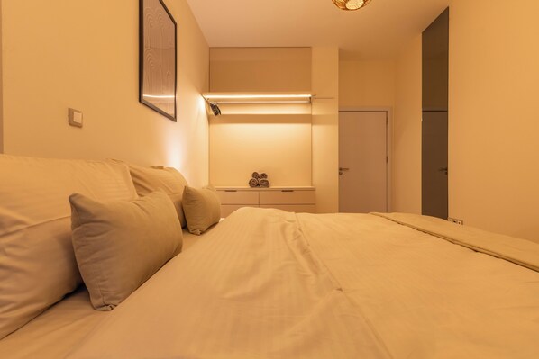 A hotel room with a bed, pillows, a bedside table, a mirror, and a door. - Prishtina City Apartments 2 (Pristina)