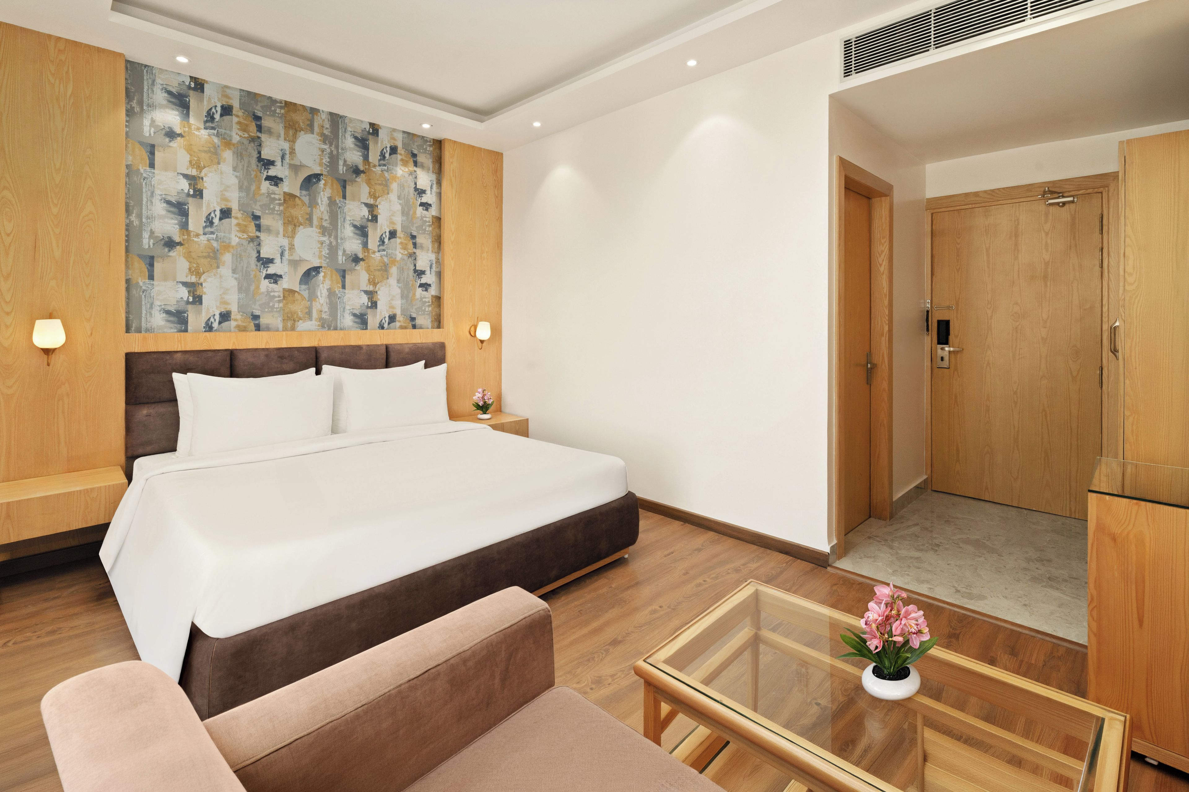 Habitación de hotel con una cama grande, un sofá, una mesa de centro de vidrio y un armario de madera.