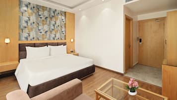 Habitación de hotel con una cama grande, un sofá, una mesa de centro de vidrio y un armario de madera.