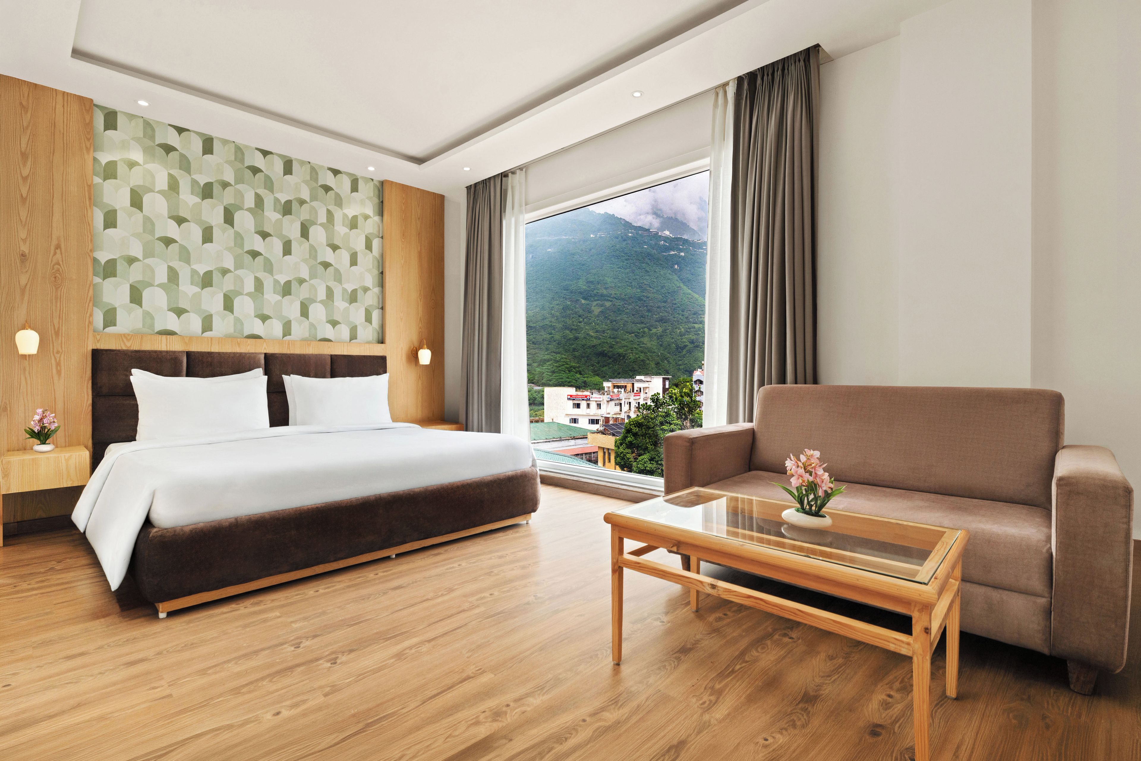 A hotel room with a bed, a sofa, a coffee table, and a view of a mountain.