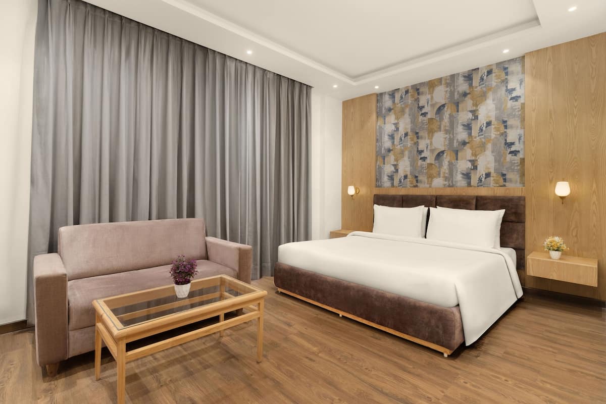 A modern hotel room with a bed, a sofa, a coffee table, and a wall with a geometric pattern.