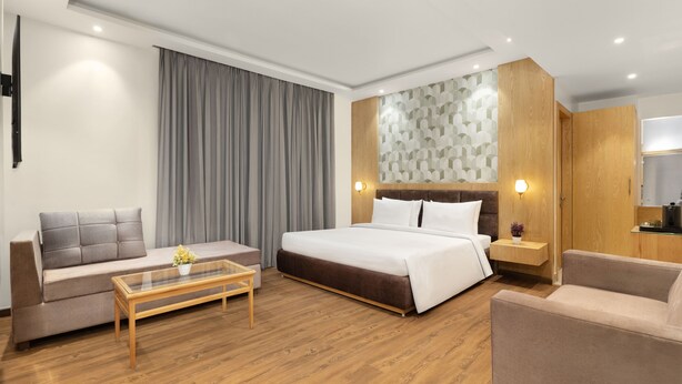 A modern hotel room with a bed, sofa, coffee table, and a small kitchen area. - Country Inn Katra (Reasi)
