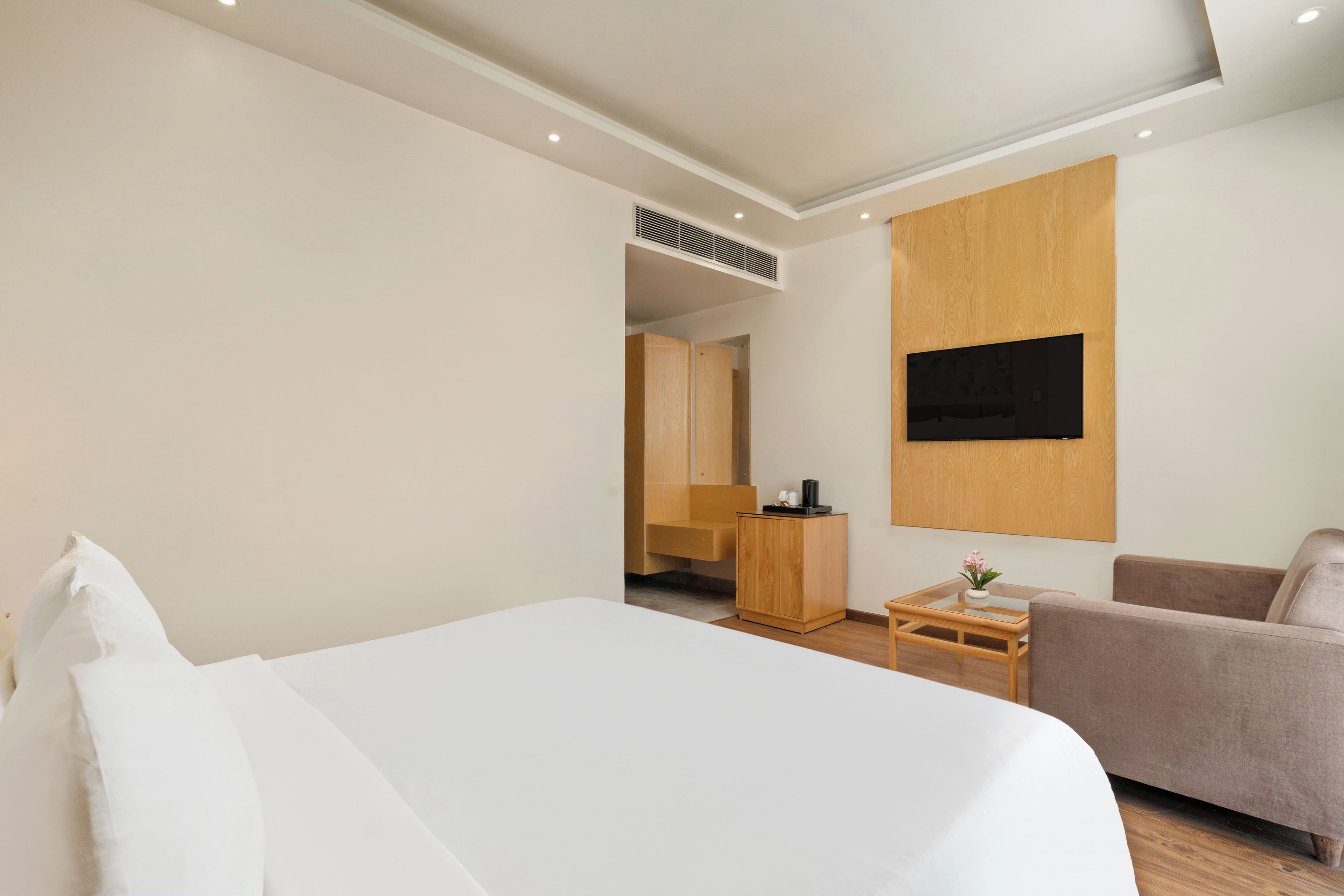 A hotel room with a bed, a seating area, a TV mounted on the wall, and a wooden cabinet.