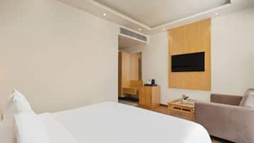 Una habitación de hotel con una cama, un área de descanso, un televisor montado en la pared y un armario de madera.
