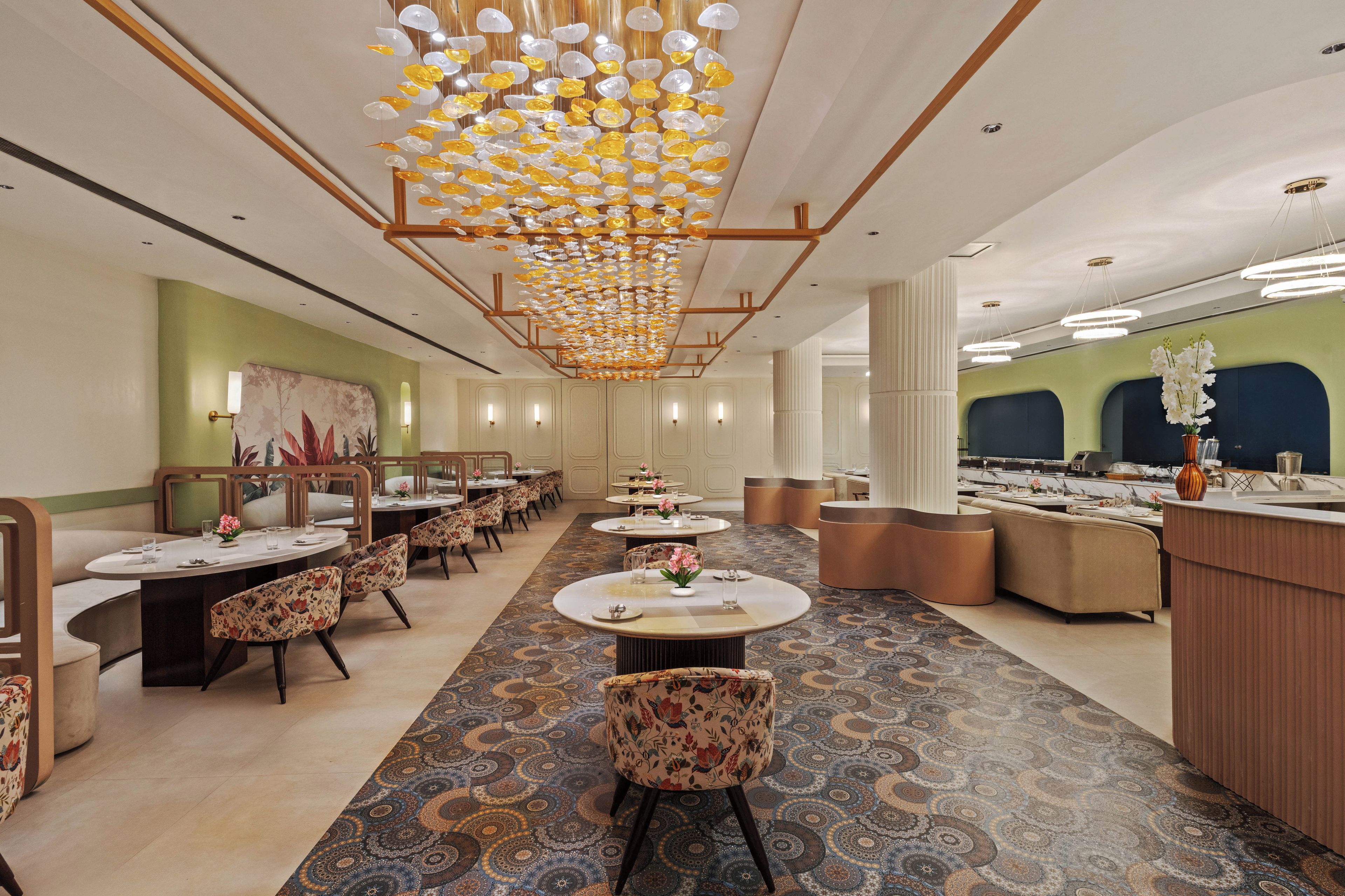 A hotel dining area with multiple round tables, chairs, and a patterned carpet.