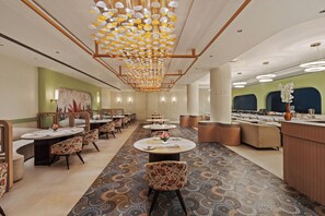 Un comedor de hotel con varias mesas redondas, sillas y una alfombra estampada.