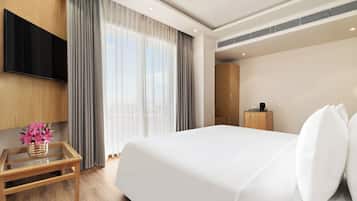 A hotel room with a large bed, a flat-screen TV mounted on the wall, a wooden nightstand with a vase of flowers, and a wooden wardrobe.